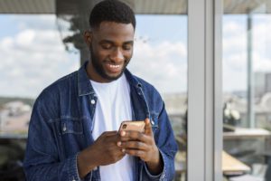 Imagem de destaque para artigo do Blog Assinei sobre assinatura digital e assinatura eletrônica. Na imagem, um homem negro jovem sorri enquanto olha para o smartphone (Créditos: Freepik)